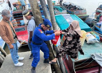 Polisi Penolong Personel Satpolairud Polres Tanjab Barat Bantu Penumpang Turun Dari Kapal di Pelabuhan LLASDP Kuala Tungkal